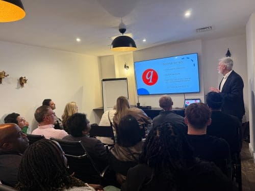 A presenter standing beside a display screen titled "Start-Up tax tips" addressing an audience seated in a presentation room.